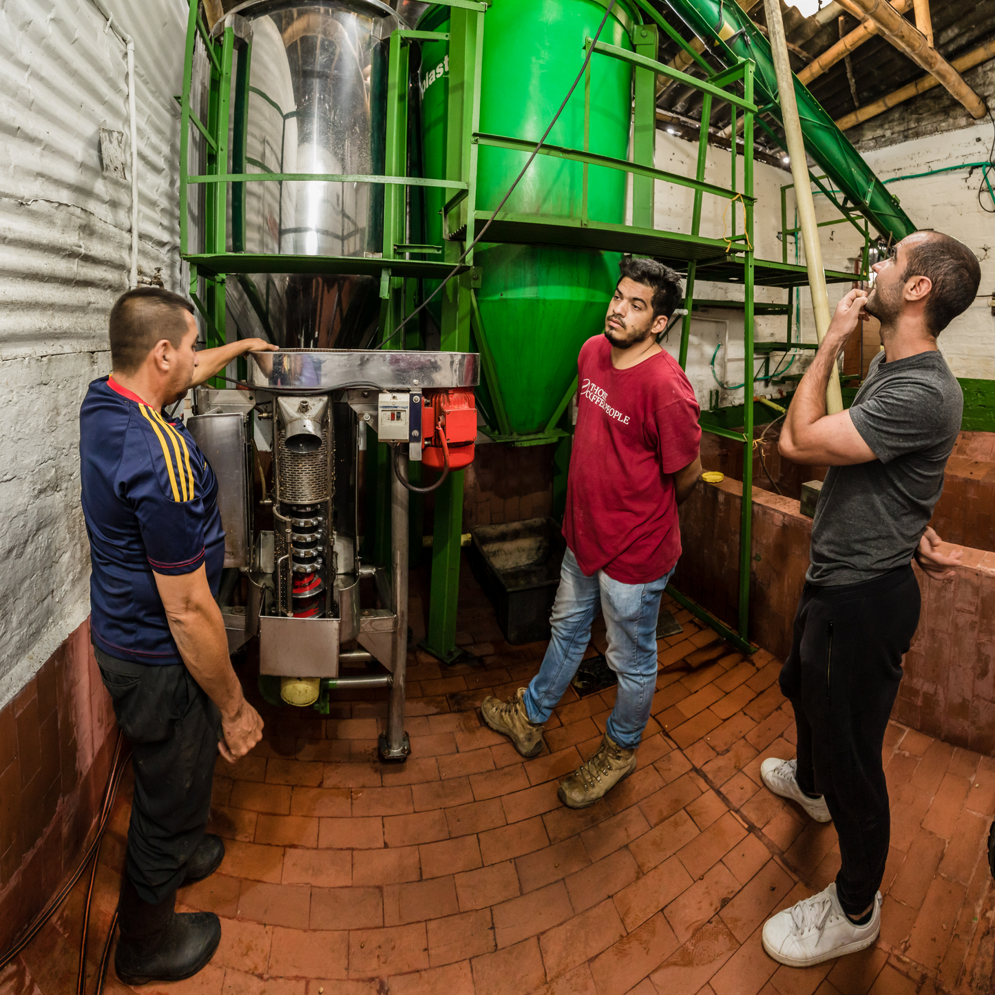 3 coffee farmers stand in front of a large green EcoMill.