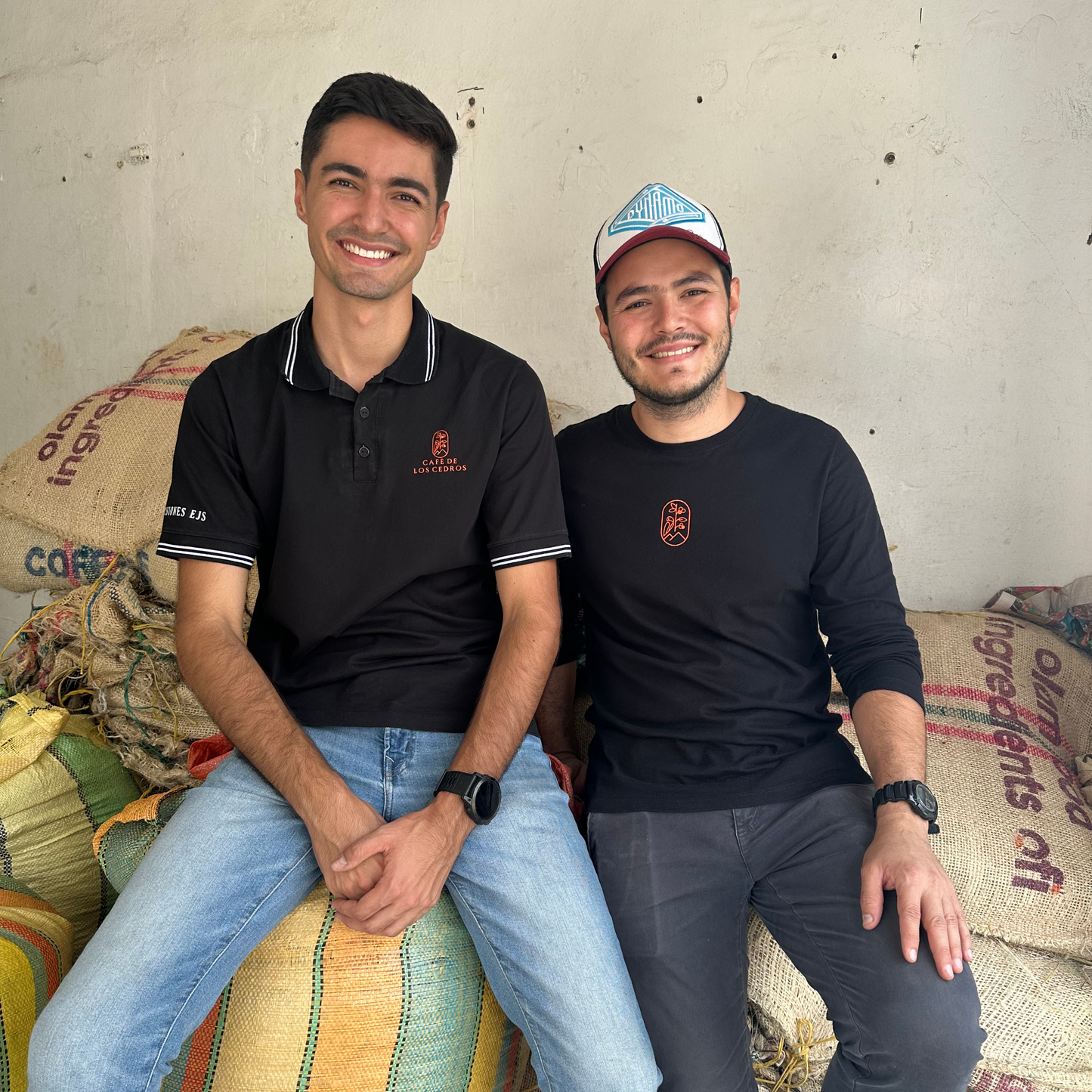 Juan David Builes and his associate, who run Los Cedros farm, sit on top of large coffee bags.