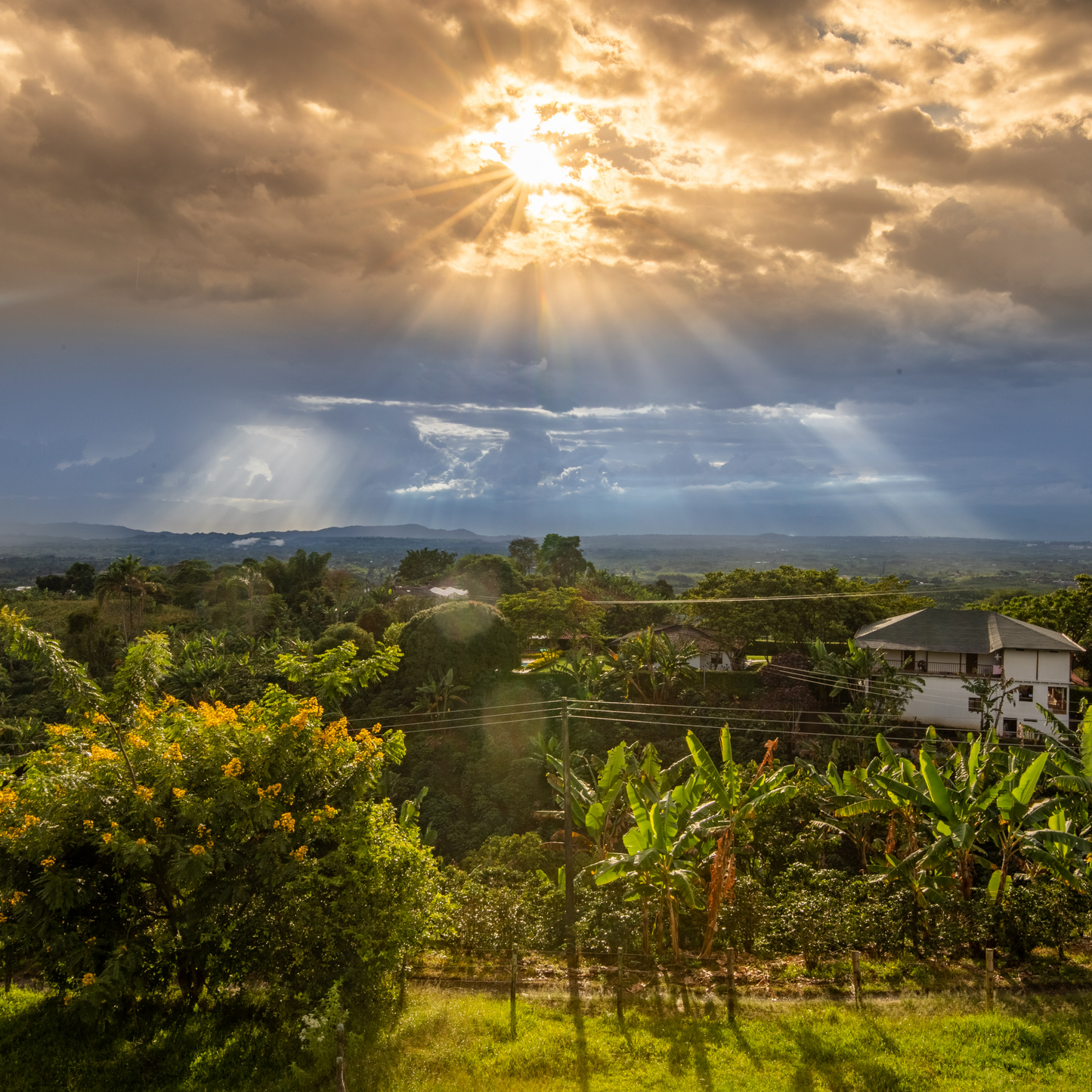 A view of the sunset from Las Brisas farm with the sun peeking through clouds to reveal a bright green mountainous landscape below.