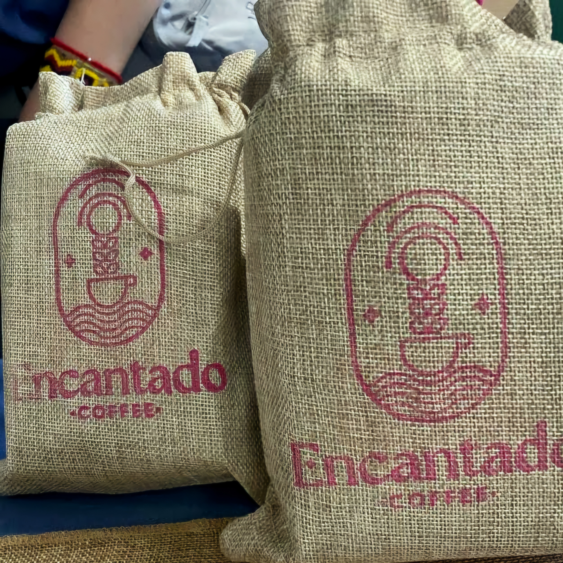 two burlap bags that are stamped with Encantado Coffee's Logo sit on a table.