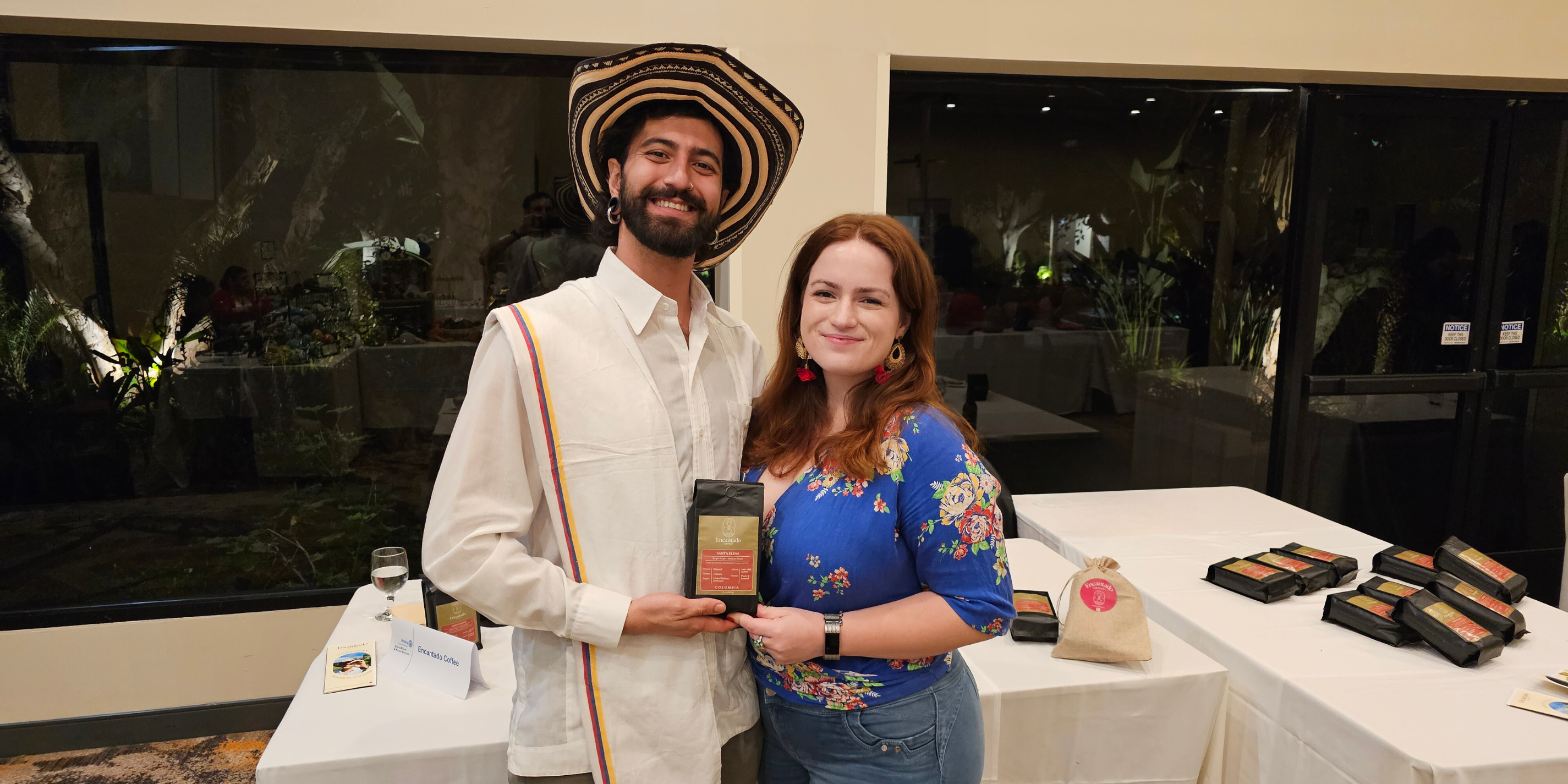 Encantado Coffee Co-Founders Sierra Roberts and Camilo Arbelaez hold a bag of Santa Elena Coffee in front of a display table at a market event.
