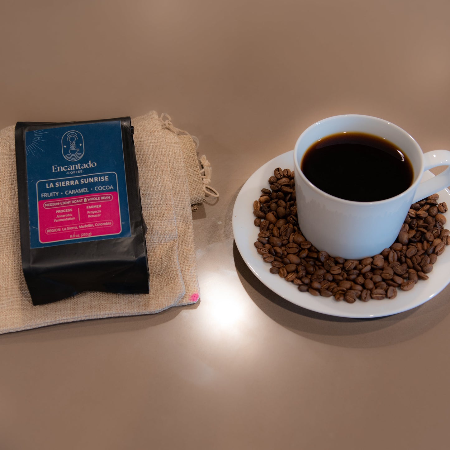 White mug with coffee on a plate of coffee beans next to a bag of coffee on a beige surface