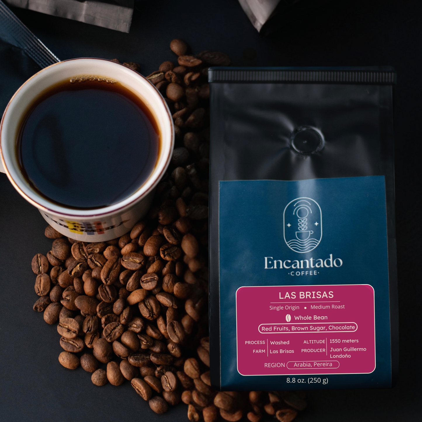 Las Brisas coffee bag lays on a black background with coffee beans and a cup of coffee next to it.