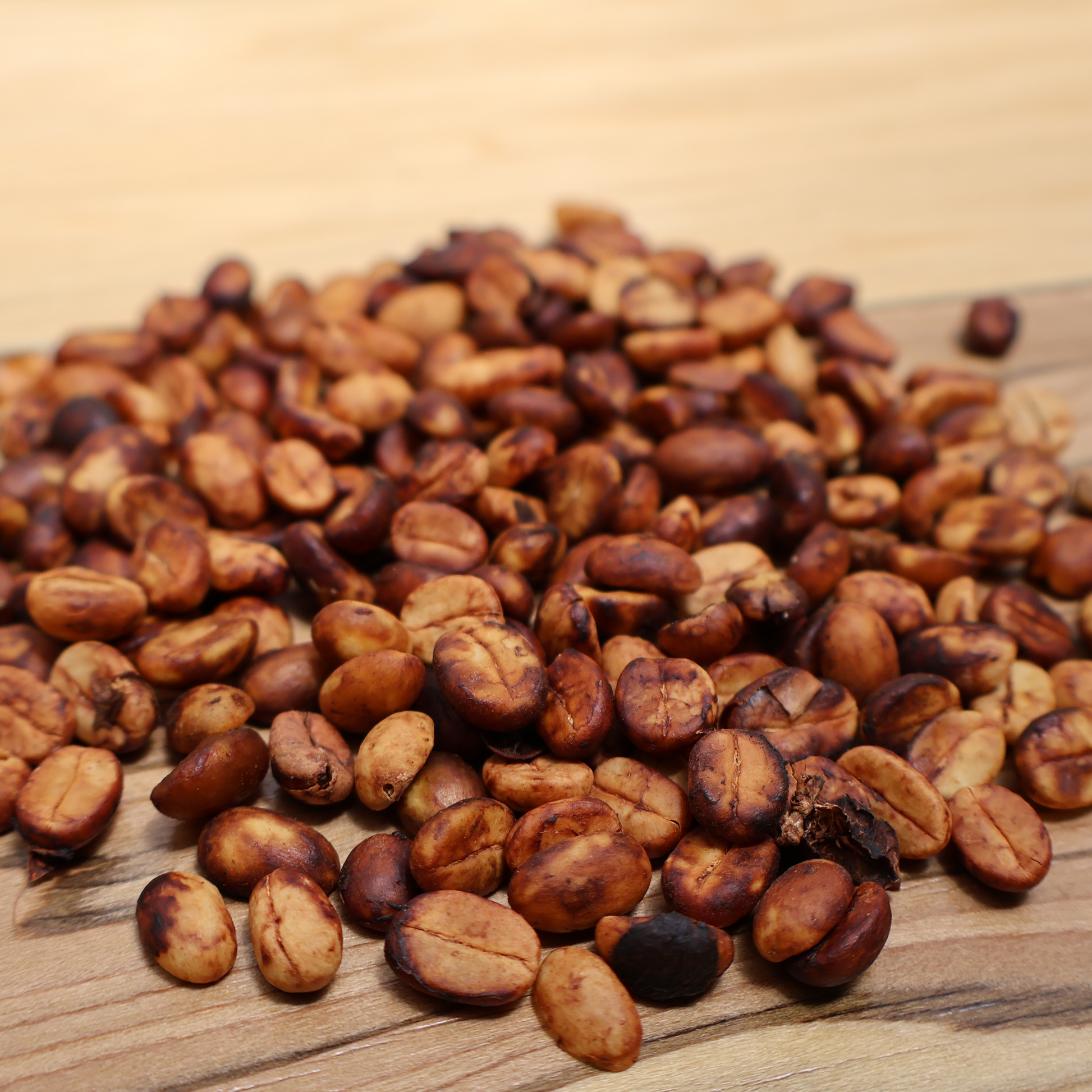 Coffee beans in their honey fermentation state, with a golden and red color, sit on a wooden table.