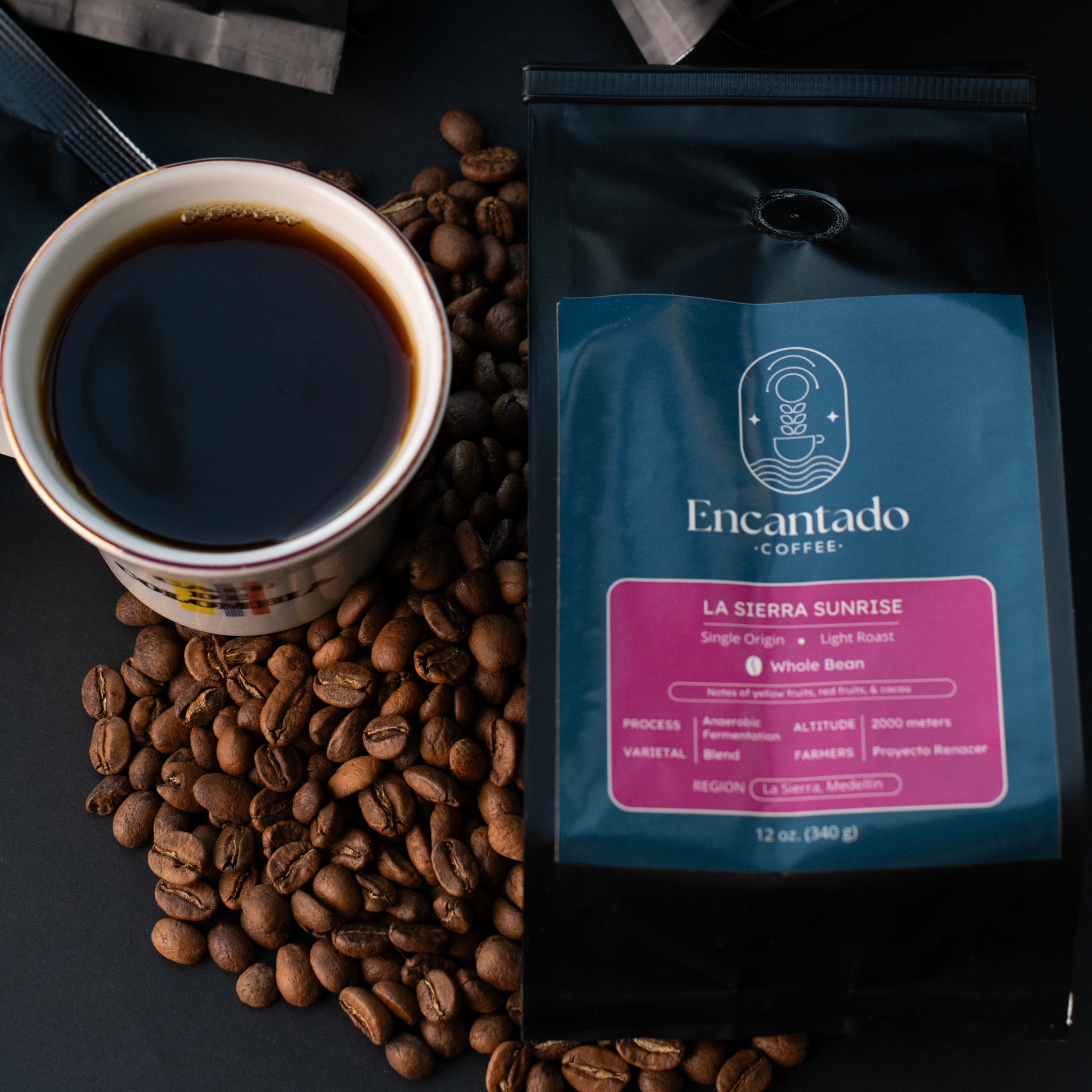 a bag of La Sierra Sunrise coffee lies on a black table next to coffee beans and a cup of coffee that says Cafe de Colombia